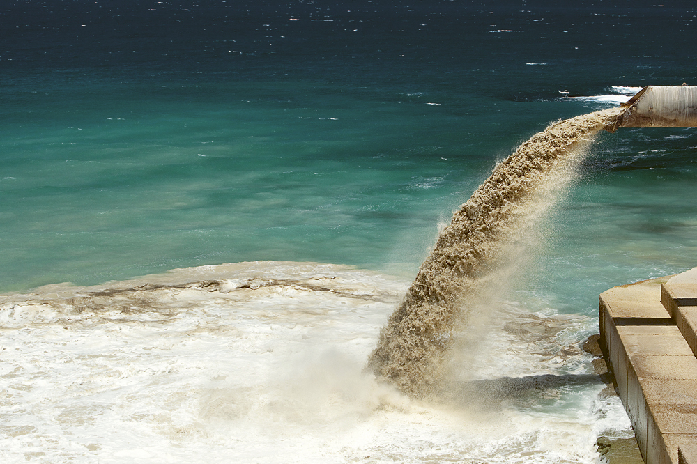 Braunes Abwasser fließt aus einem Rohr ins Meer