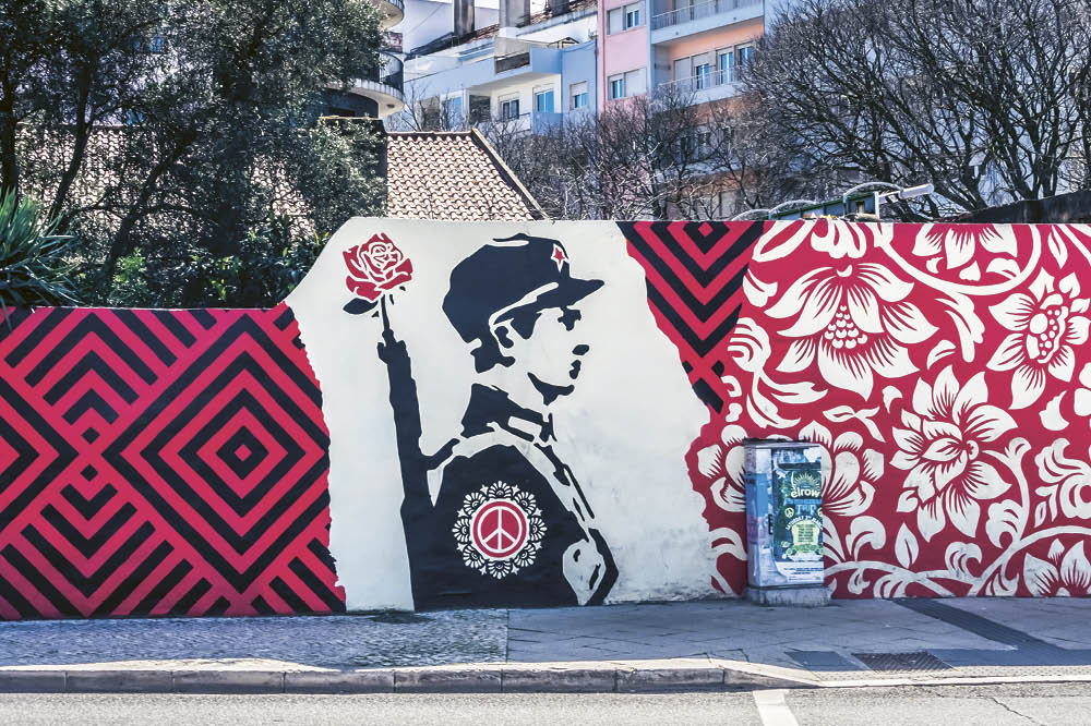Eine Wand voller Graffiti mit einem Bild von einem Soldaten in der Mitte von roten Blumen umgeben. 