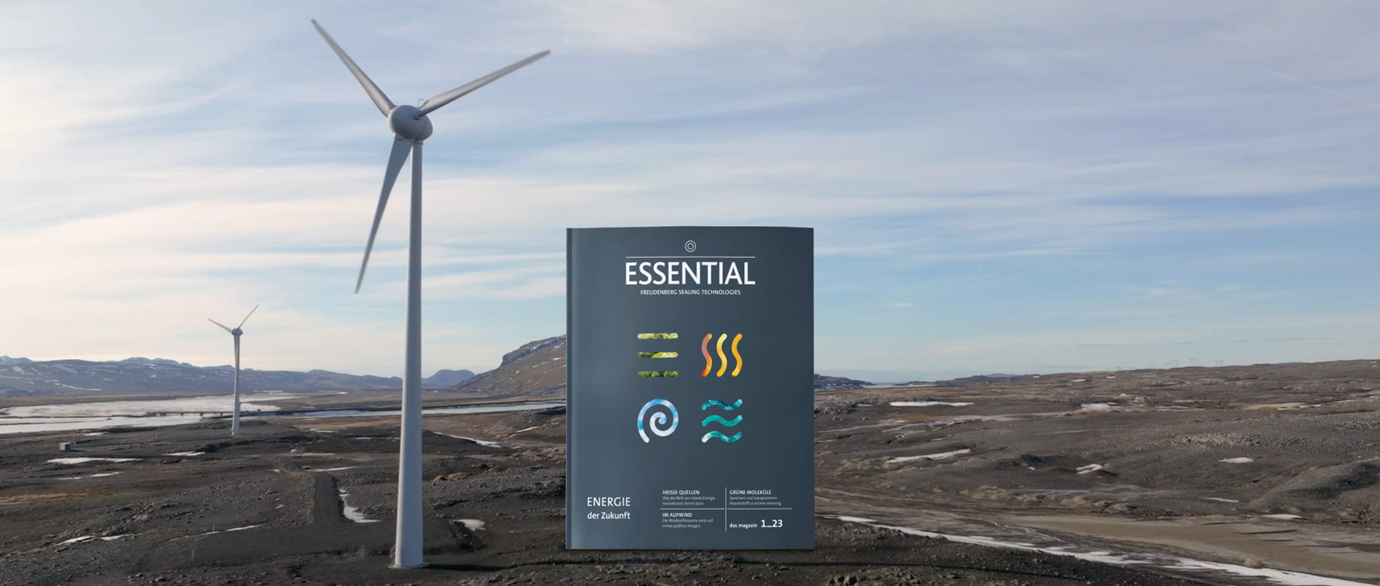 Das ESSENTIAL-Magazin mit dem Thema erneuerbare Energien steht neben einem Windrad in der Landschaft.