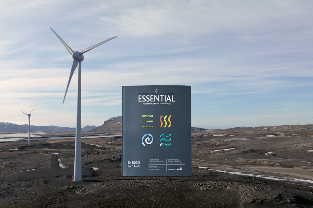 Das ESSENTIAL-Magazin mit dem Thema erneuerbare Energien steht neben einem Windrad in der Landschaft.