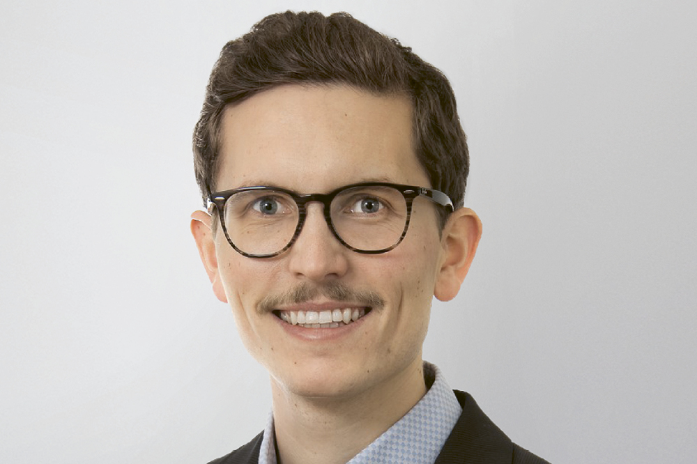 Portraet eines Mannes mit einer schwarzen Brille und einem Schnurrbart. 