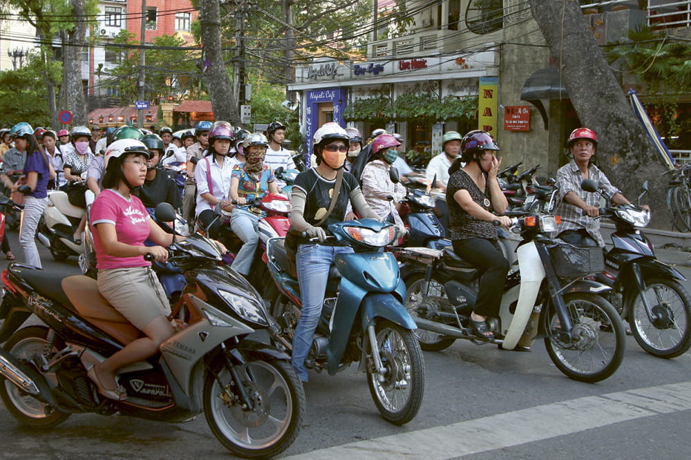 Eine Schar von Rollerfahrern stehen an einer Kreuzung.