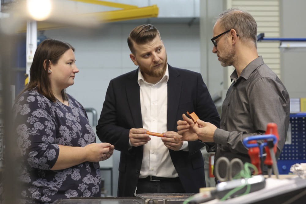 Eine Frau und zwei Männer, Kira Truxius, Marco Sutter und Björn Hellbach, halten ein Stück des Hochleistungskunststoffs Quantix® ULTRA in den Händen und sind in ein Gespräch vertieft.