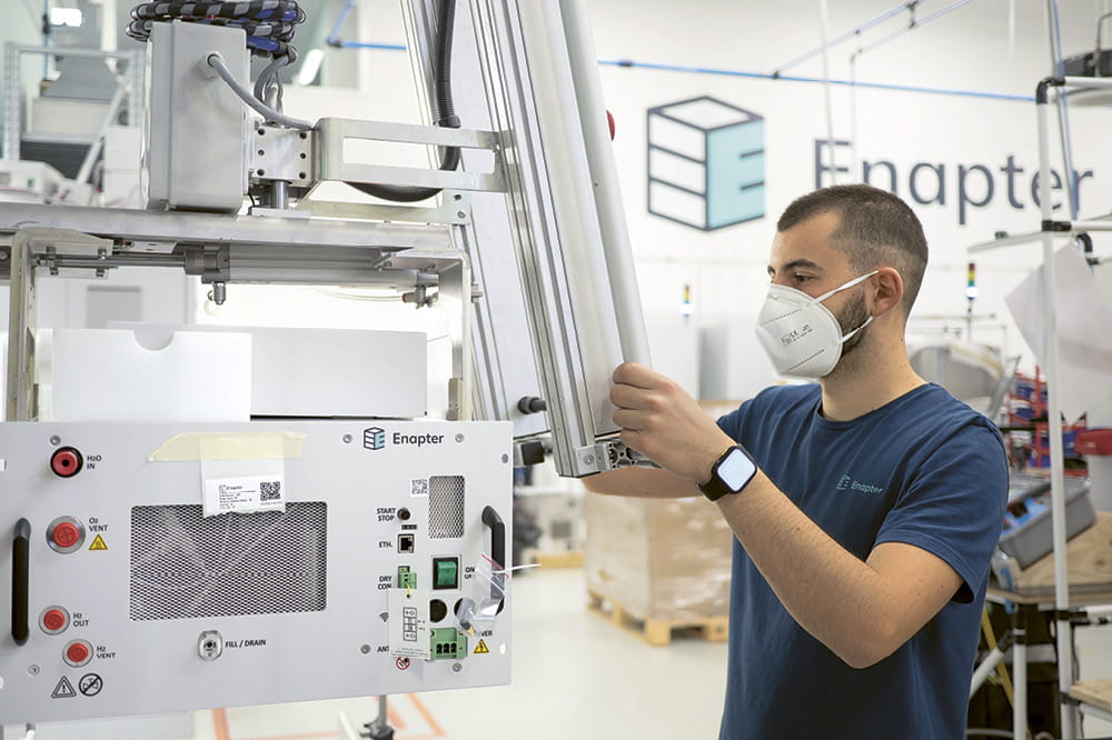 Ein Mann mit Maske schaut auf einen Bildschirm in einer Fabrik.