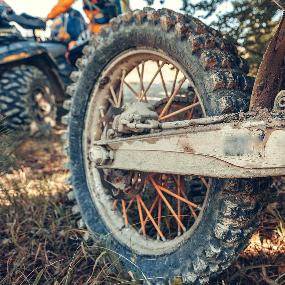 Nahaufnahme eines matschigen Motorcross-Rads auf einer Wiese und einem Quad im Hintergrund 