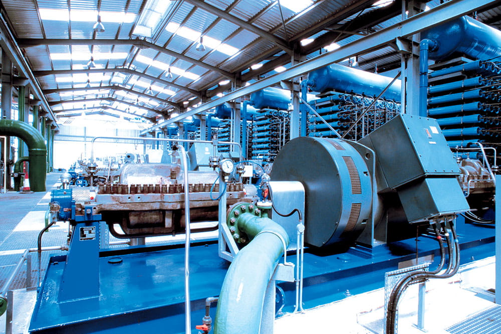 Innenansicht eines Industriekraftwerks mit Generator und Turbinenmaschinen, Hochleistungs-Pumpensystem, Stahlrohren, Manometern und Wärmetauschereinheiten in einer modernen Fabrikhalle mit Metalldachkonstruktion 
