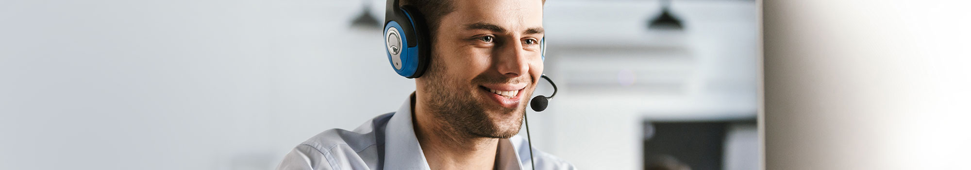Call Center Mitarbeiter mit Headset vor einem Computer und weiterem Mitarbeiter im Hintergrund